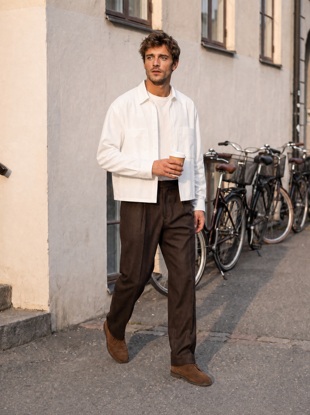 Man in wit cropped overhemd loopt met koffie door een straat met fietsen